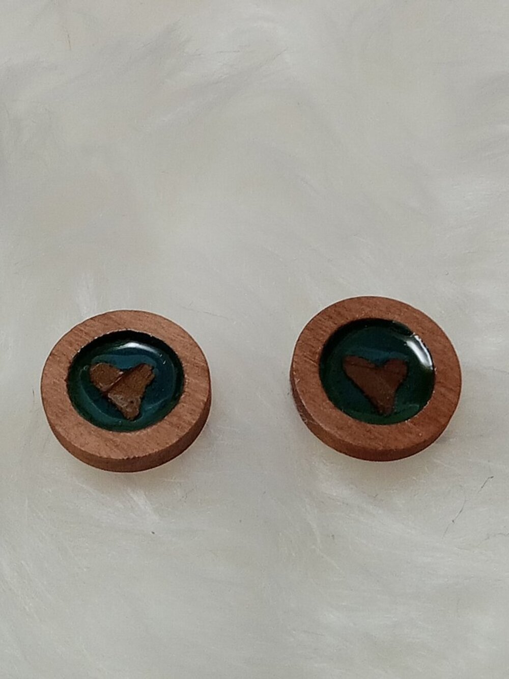 Handmade earrings on a wooden base with a piece of punched-out tree leaf